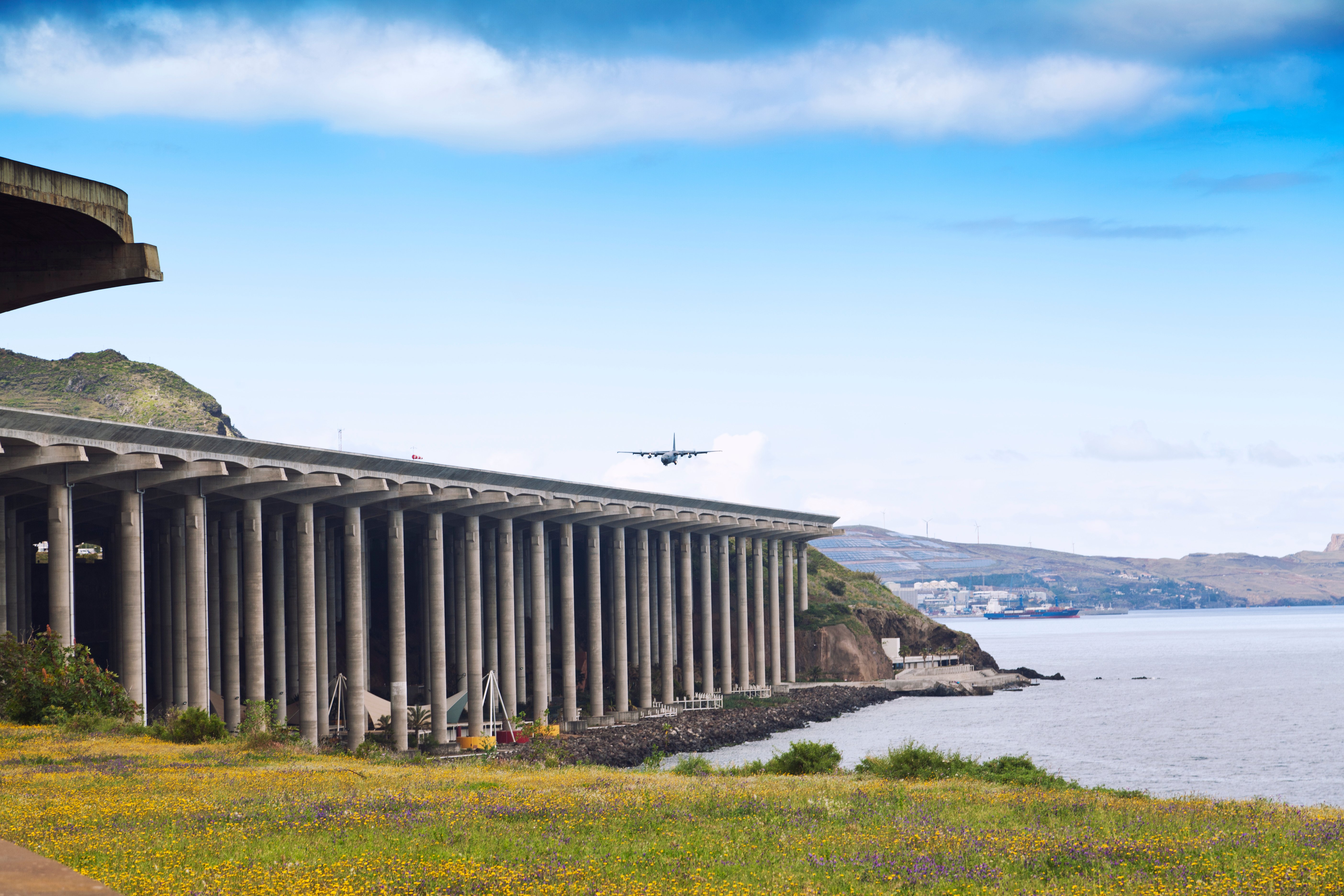 Aircraft approaching Madeira Airport with runway extension supported by concrete pillars over the ocean.