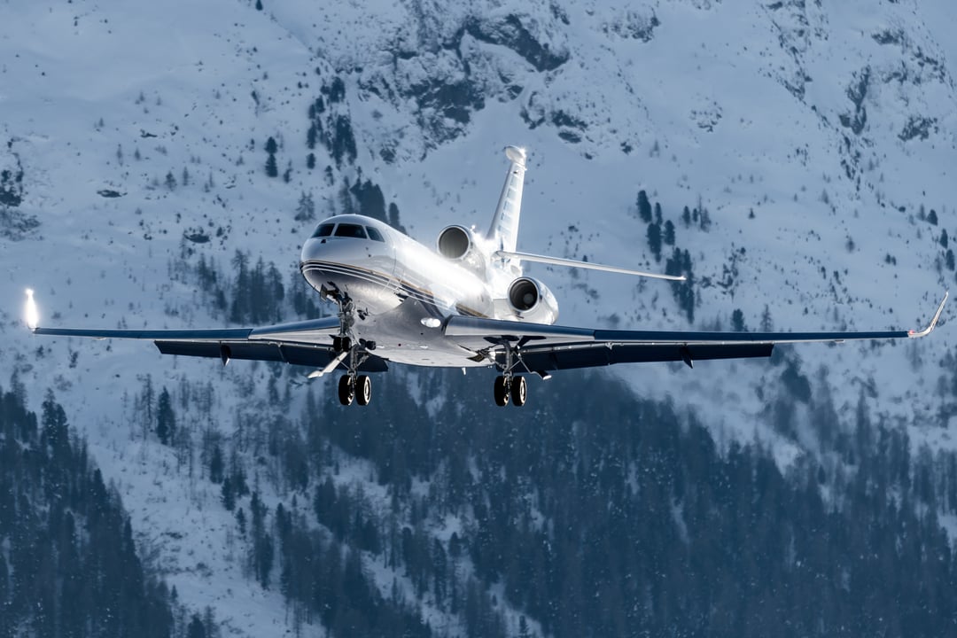 Business jet on final approach over snowy mountainous terrain, illustrating winter operations and the challenges of planning for wet and contaminated runway conditions.