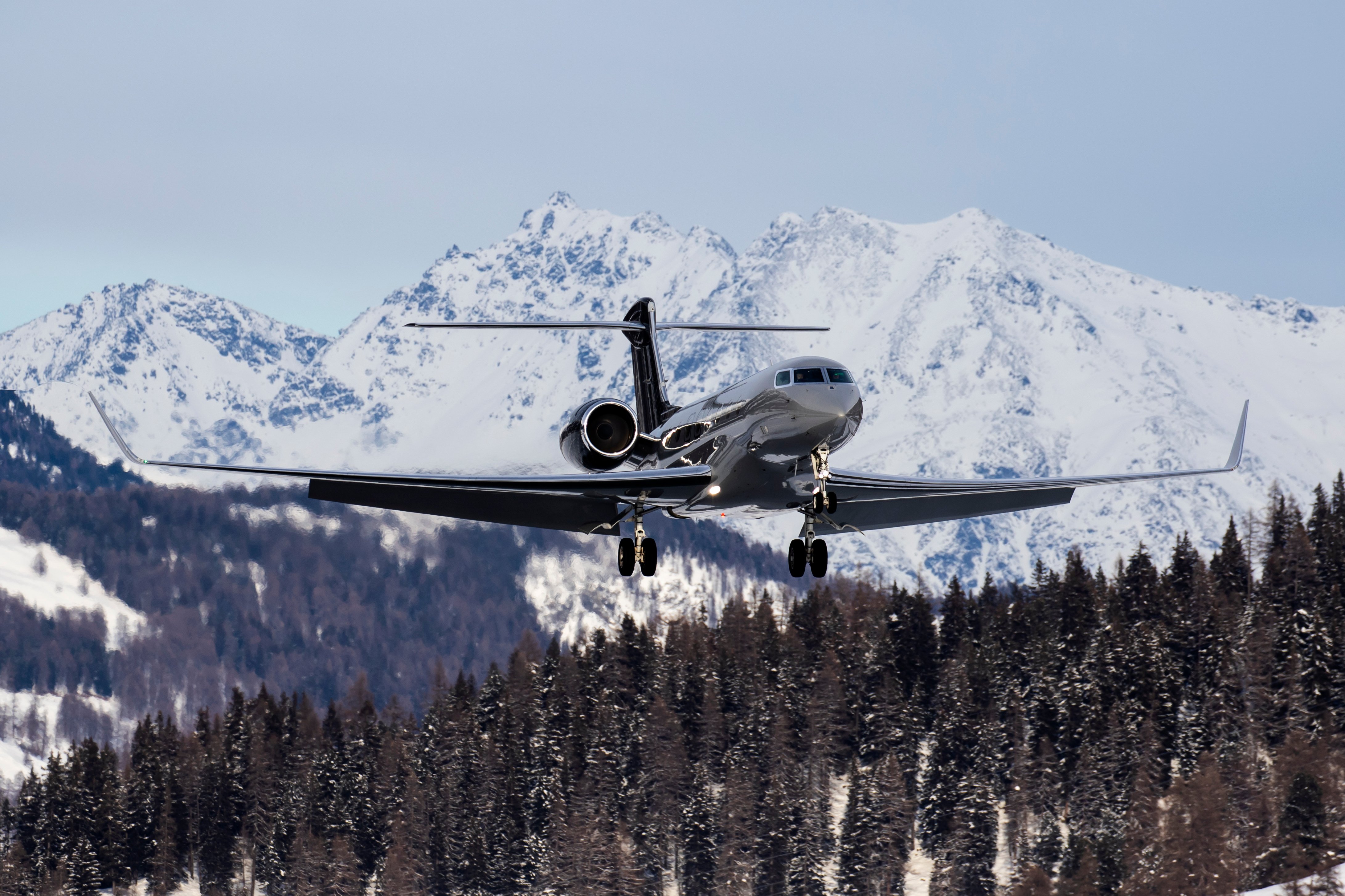 Business jet on approach over snow-covered terrain with mountains in the background, illustrating the challenges of winter operations and contaminated runway conditions.