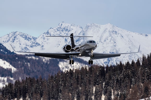 Business jet on approach over snow-covered terrain with mountains in the background, illustrating the challenges of winter operations and contaminated runway conditions.