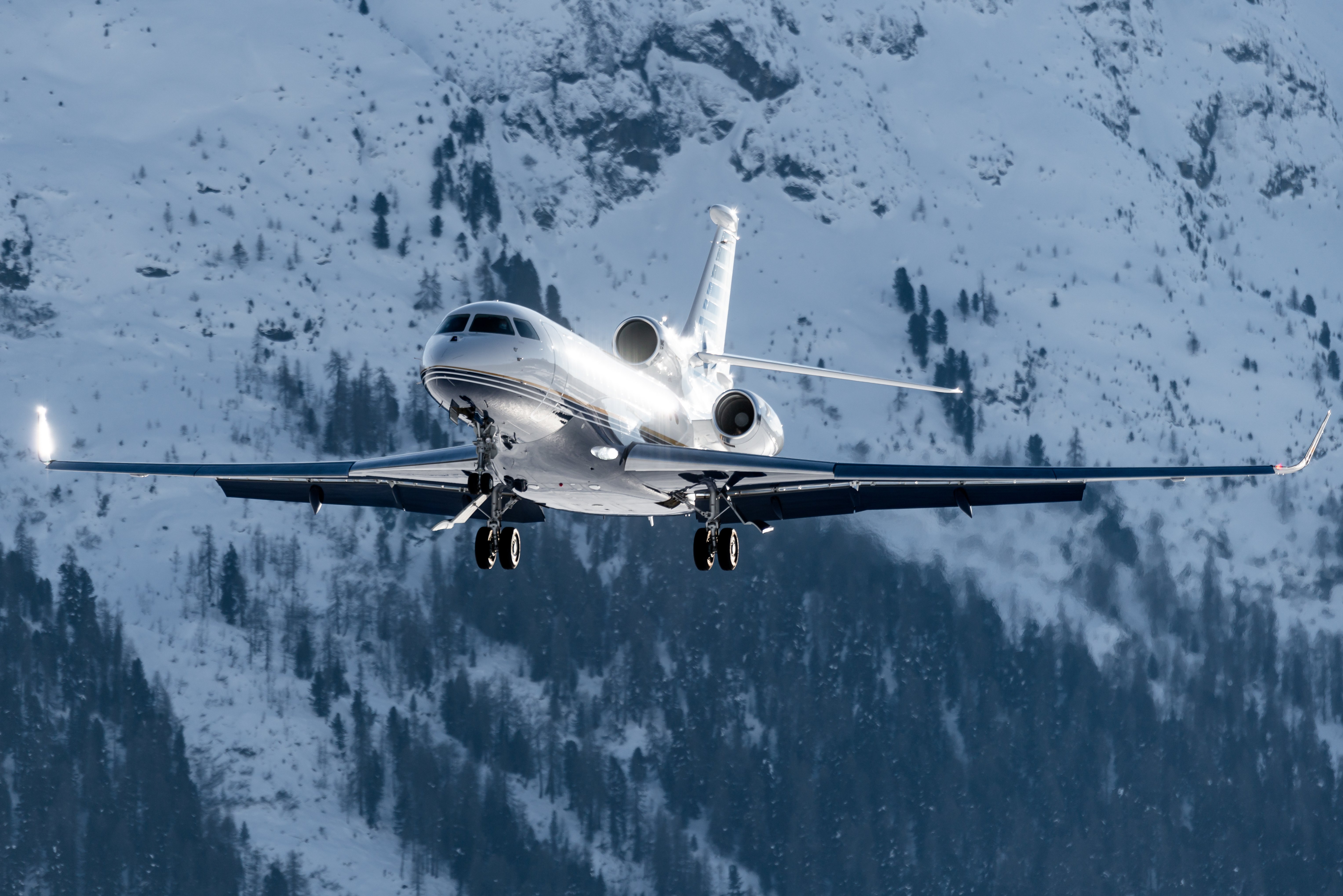 Business jet on final approach over snowy mountainous terrain, illustrating winter operations and the challenges of planning for wet and contaminated runway conditions.